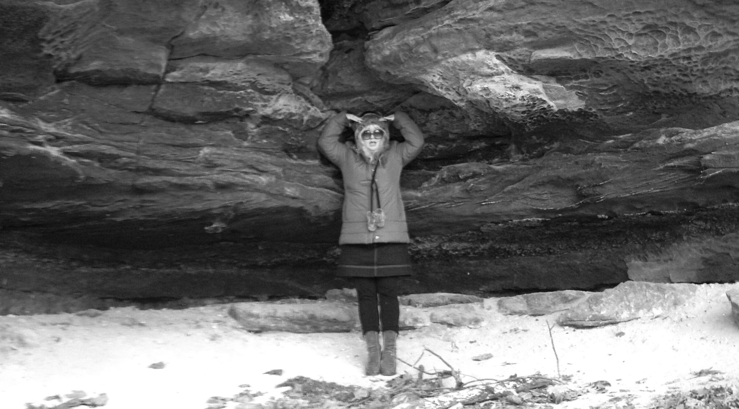 Woman posing under a rock overhang, holding hands above head.