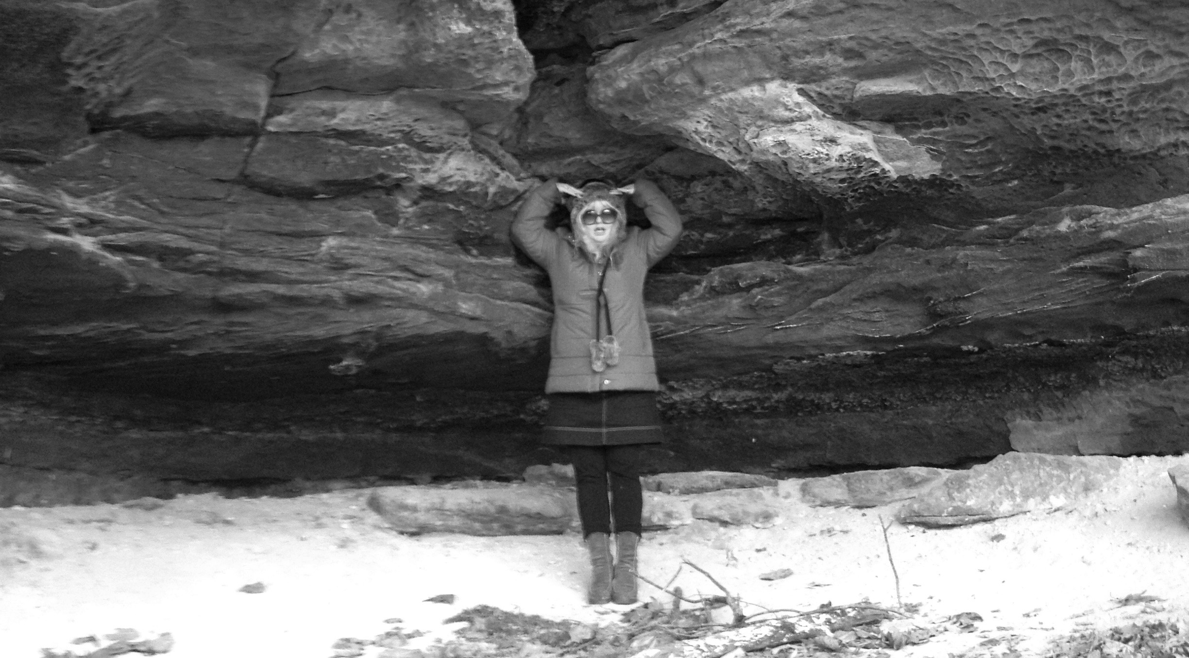 Woman posing under a rock overhang, holding hands above head.