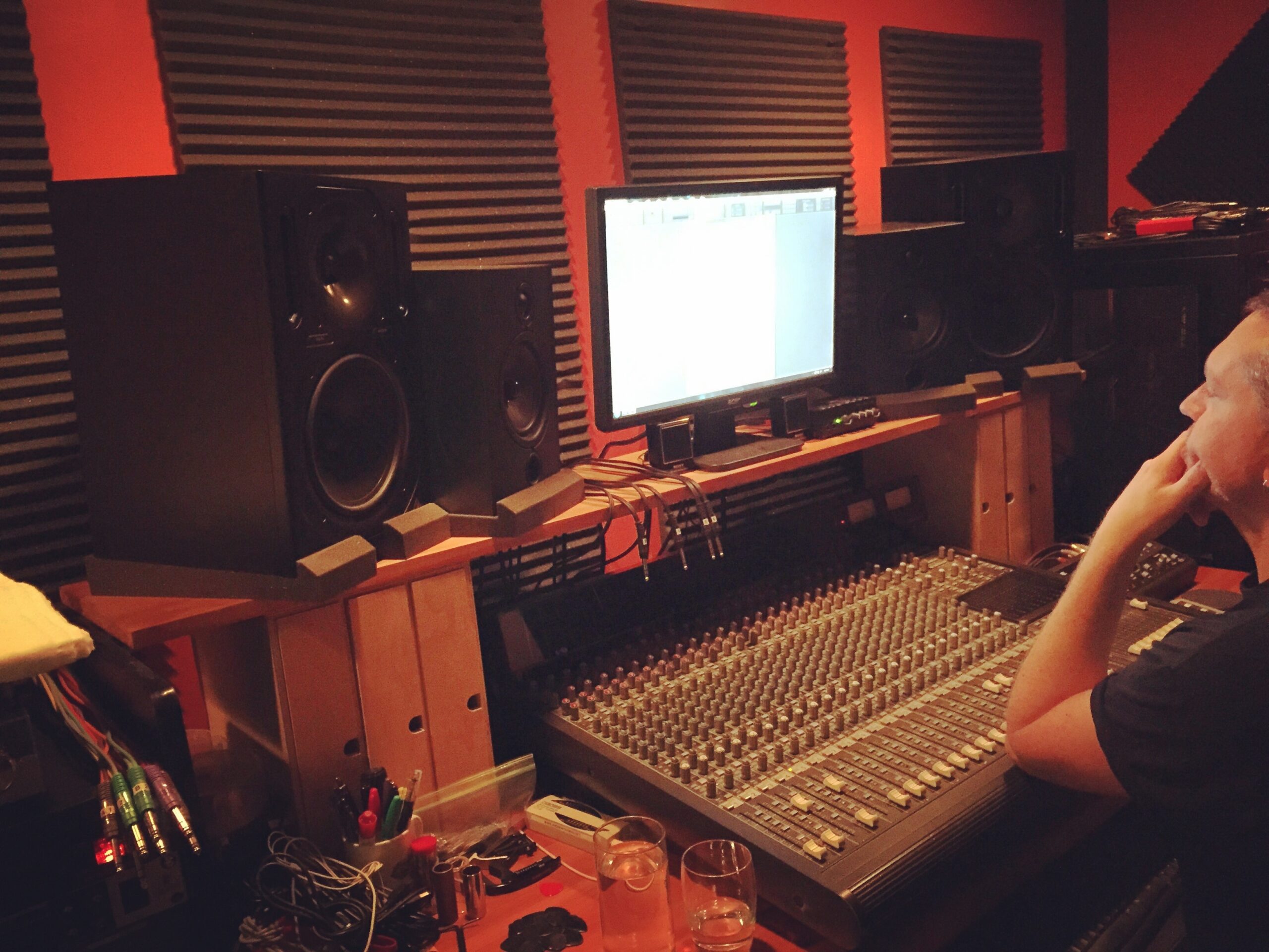 Man at soundboard in recording studio with speakers and monitor.