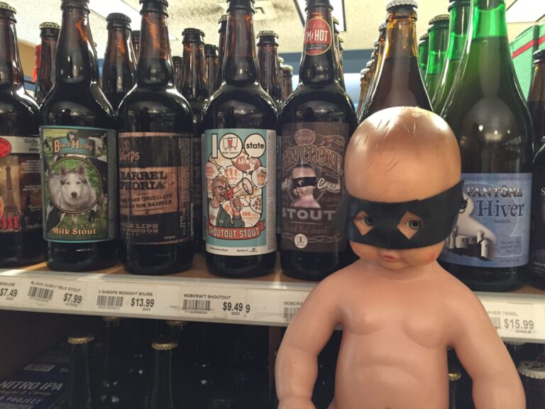 Doll with black mask in front of beer bottles.