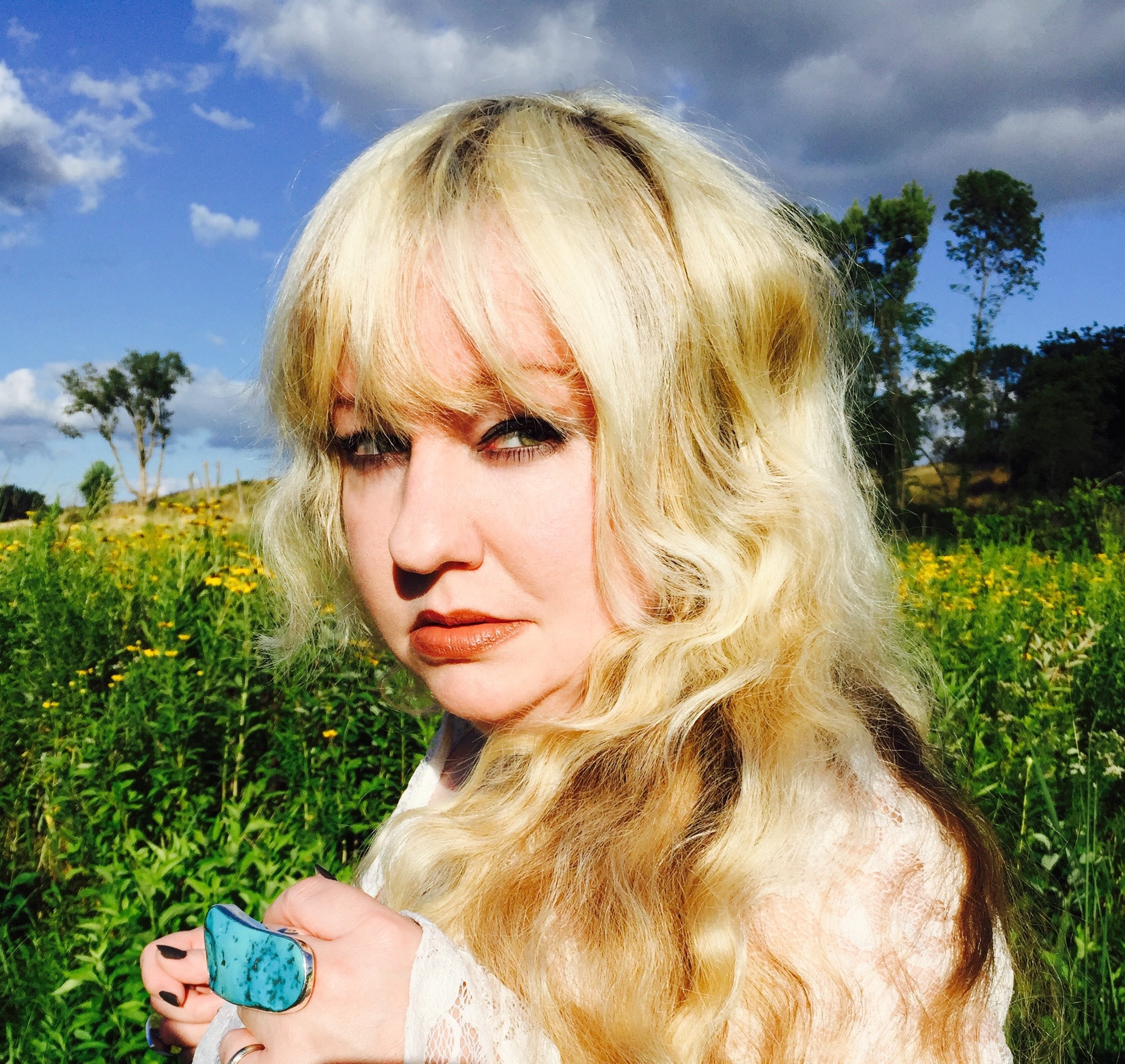 Woman with blonde hair and large turquoise ring in a field of yellow flowers.