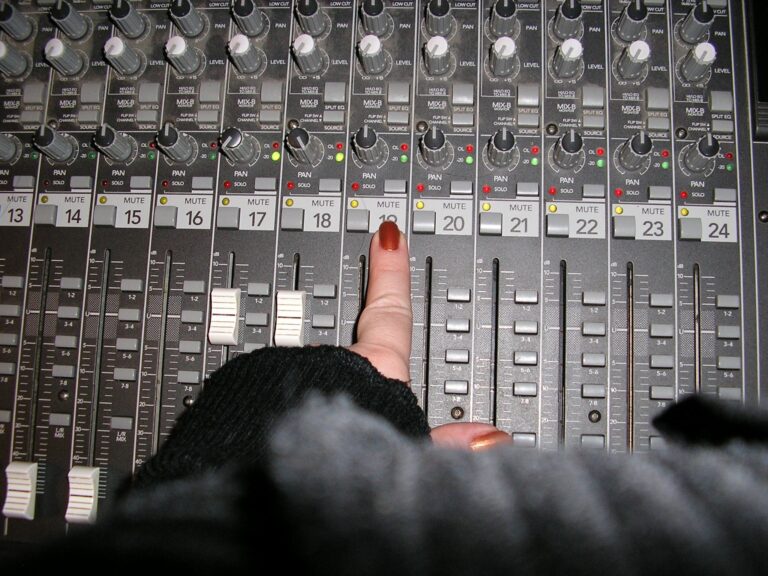 Finger presses mute button 19 on a sound mixing board.