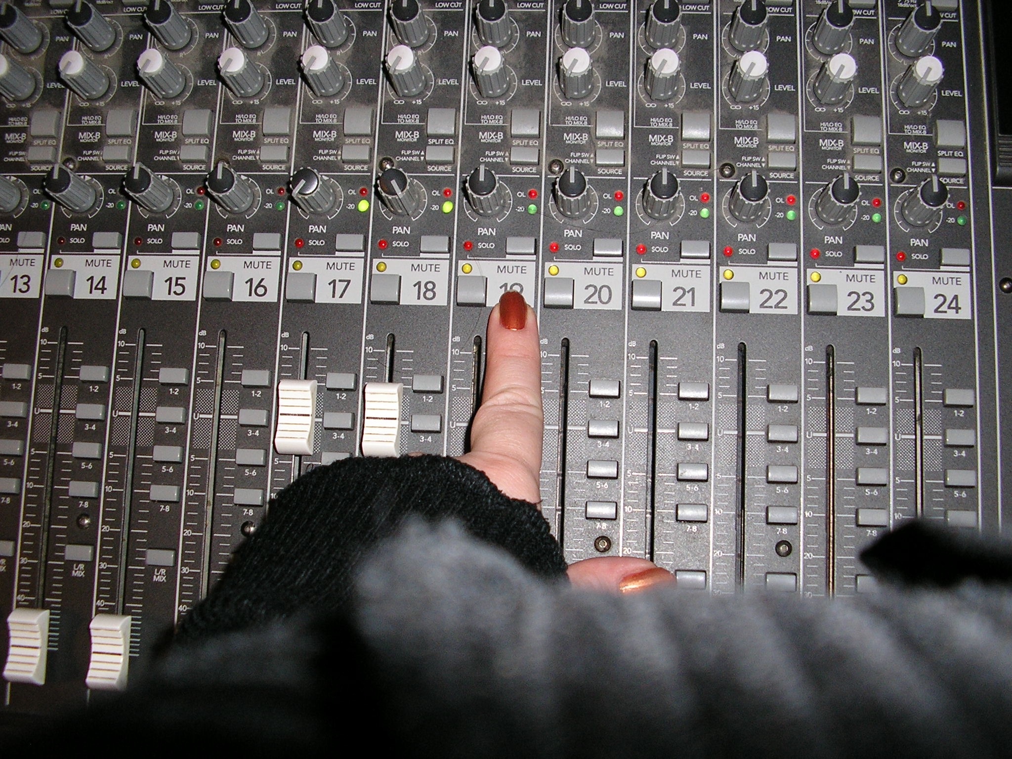Finger presses mute button 19 on a sound mixing board.