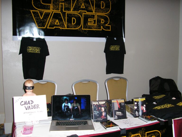 Chad Vader merchandise display with t-shirts, DVDs, and a laptop.