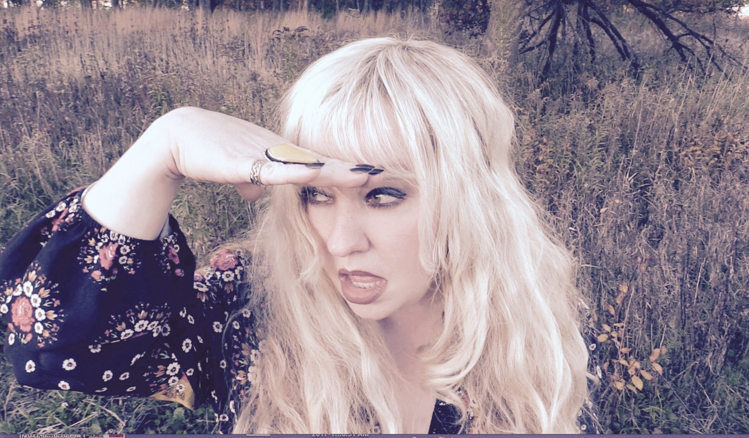 Woman with blonde hair shielding eyes, wearing floral dress in a field.