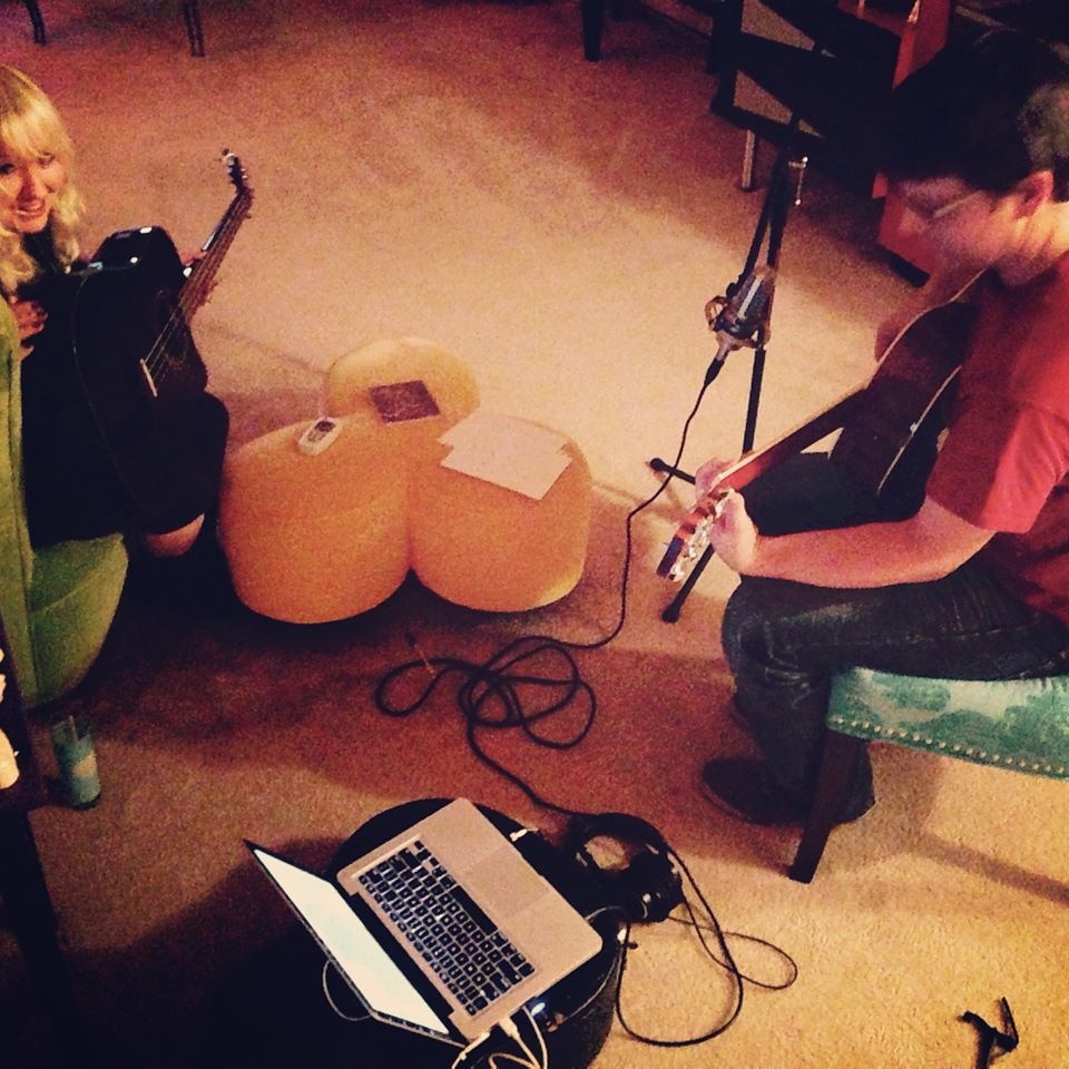 Two people playing guitars with a laptop and microphone setup.