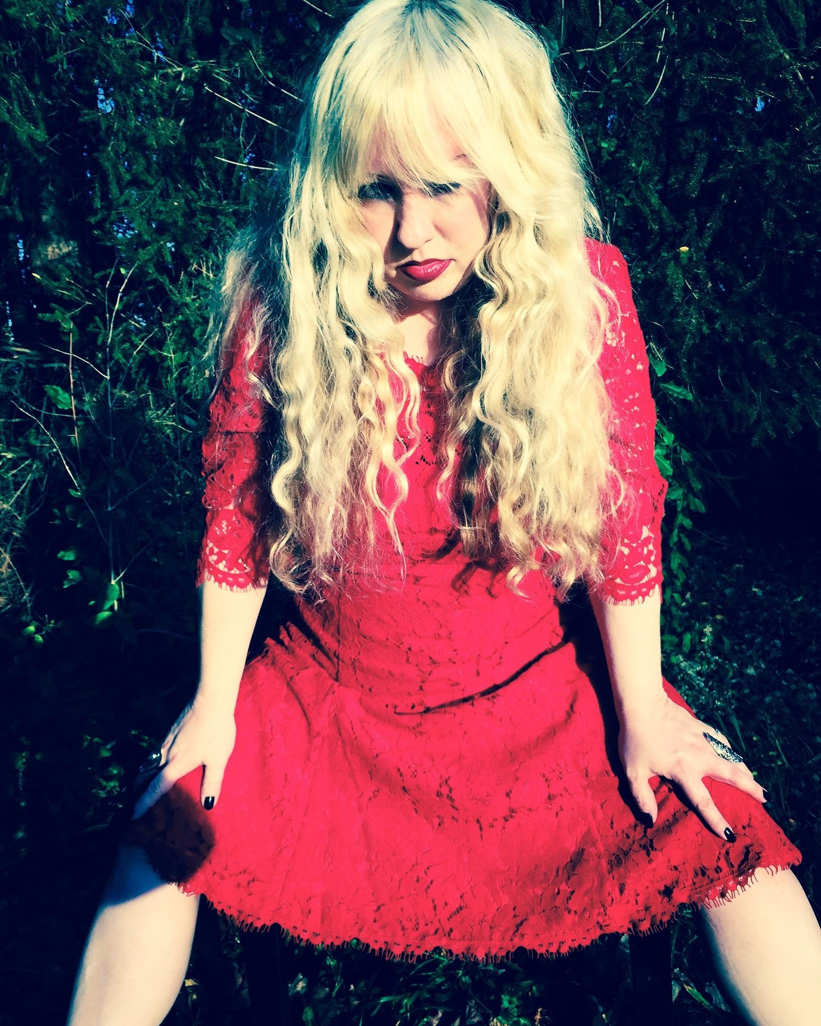 Woman with long blonde hair in a red lace dress, posing outdoors.