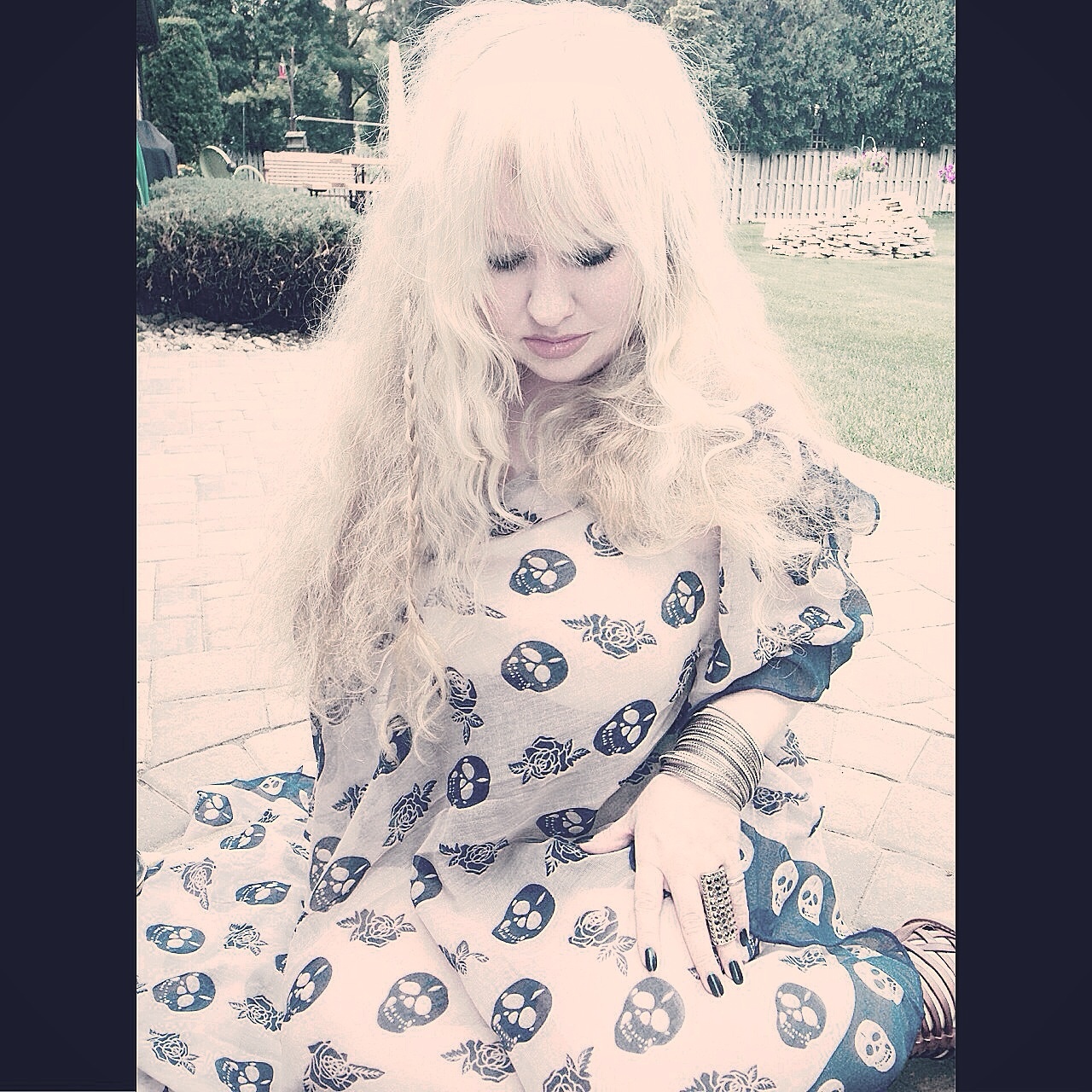 Woman with long blonde hair wearing a skull-print dress and bangles.